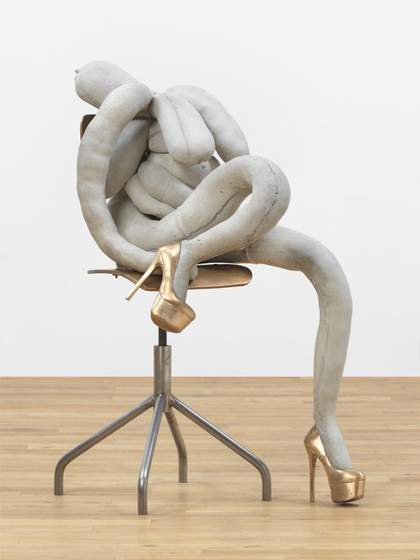Grey concrete cast of soft tangled tubular limbs slumped in a knot on a steel swivel chair, one long leg trailing to the floor, its feet in shiny gold platform stiletto shoes