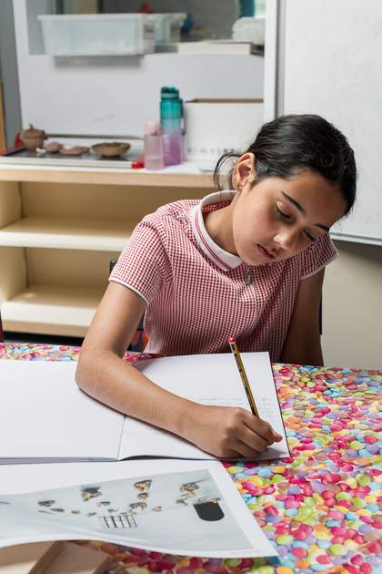 A young person sits at the table writing in their notebook as they look at a printed out image of the artwork.