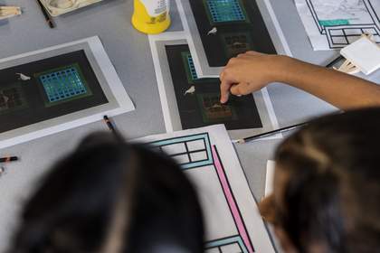 An overhead shot of students looking at Parviz Tanavoli’s ‘Cage, Cage, Cage’ printed out in multiple copies on their table. One student points to the cage at lower centre.