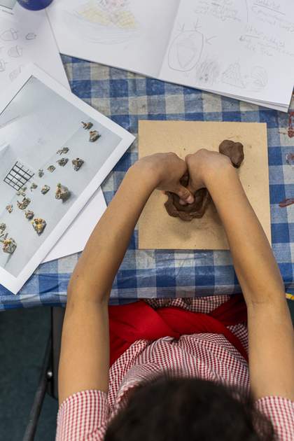 An overhead shot of a young person shaping their clay vessel. They push their thumbs into a hollowed-out bowl shape.