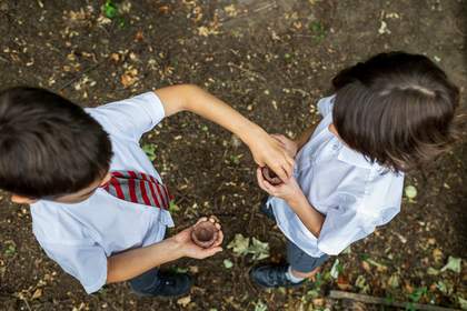 An overhead shot of two students holding their vessels in their hands. The student on the left reaches out to touch the top of the student on the right’s vessel.