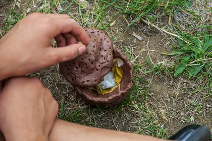 A student puts a lid on their vessel after filling it with a feather, some leaves, and a maple key. The lid has a dotted pattern made by perforating the clay with holes.
