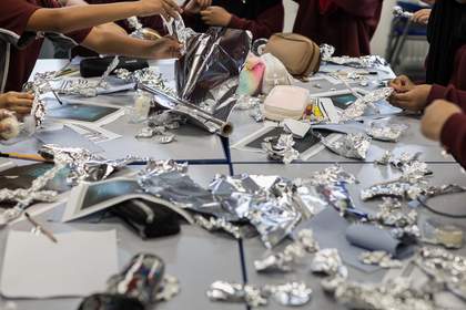 Students sit around a table and manipulate sheets of tinfoil. On the table are multiple scrunched up pieces of tinfoil, as well as tinfoil birds and other figures.