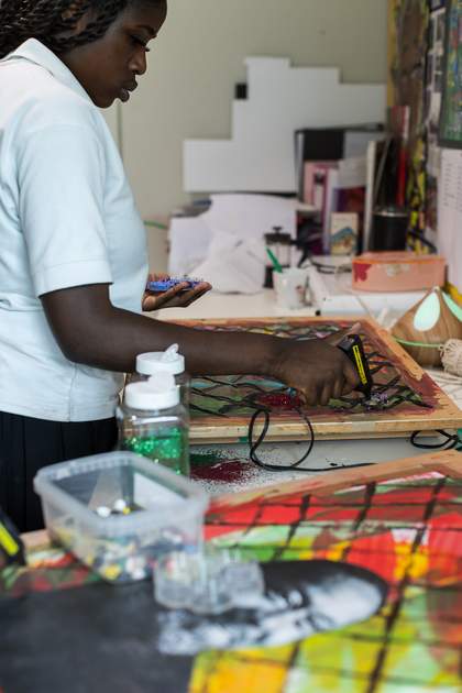 A student uses a glue gun to affix beads to their artwork.