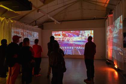 A photograph of a group of people standing in a dimly-lit room watching a projection on the wall.