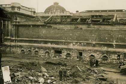 Sepia photo of the exterior of Tate Britain, a few people are looking at the bomb damage.