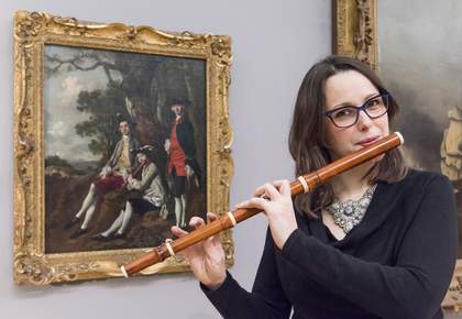 Hannah French poses with a replica of a baroque flute in front of Thomas Gainsborough’s Peter Darnell Muilman, Charles Crokatt and William Keable in a Landscape c.1750