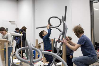 boy making artwork from grey pipes with artist