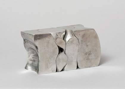 A silver sculpture, shaped like a segmented block, against a white background