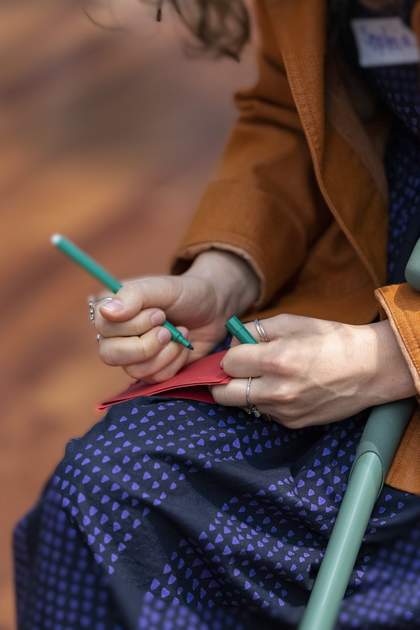 A person holds a green marker in their right hand. It hovers above a red piece of paper on their lap.