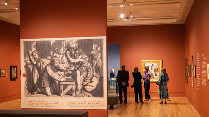 I painting in the foreground of a gallery space with people looking at a different painting in the background.