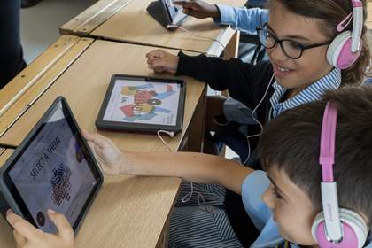 A group of students with headphones on are interacting with the LIGHTBOX resource on tablet devices.