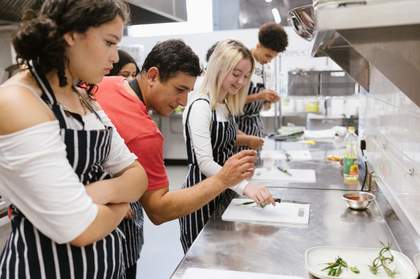 A photograph of young people and a chef preparing plates of food in a kitchen.
