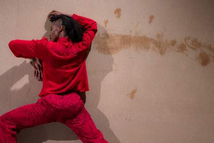 Dancer Yinka Esi Graves performing against a wall wearing red trousers and red shirt.