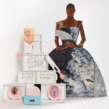 on the left, a figure with blonde hair and a pearl necklace assembled from white painted boxes; on the right, a wooden painted cut out of a person in a ball gown