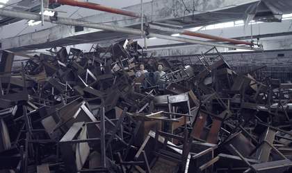 a huge pile of abandoned wooden desks and chairs, all broken on top of each other. 