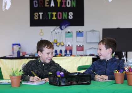 Two boys sitting at a craft table laughing at each other