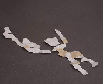 Sculpture of a rudimentary figure made from aluminium and acrylic paint, which has been made to look like torn fragments of white paper lying on the floor.