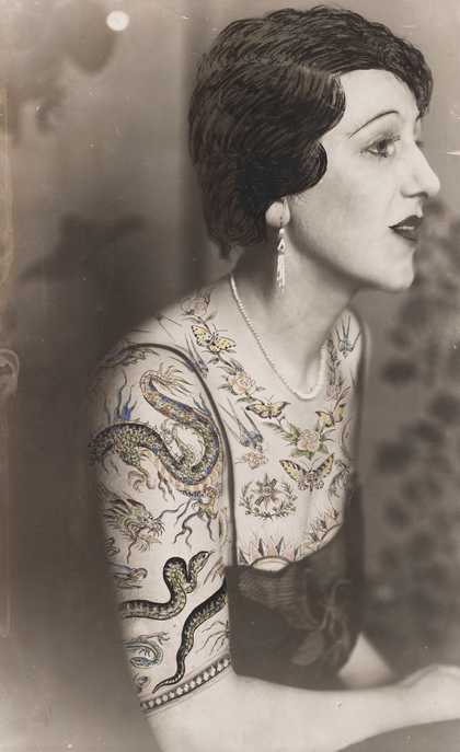 Black and white photograph of a woman sitting in profile, the bust dressed in a blouse made of tattoo patterns drawn on the photograph