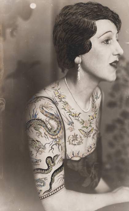 Black and white photograph of a woman sitting in profile, the bust dressed in a blouse made of tattoo patterns drawn on the photograph