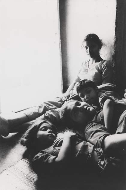 Three figures lie on the floor in an embrace, while another sits against a nearby wall.