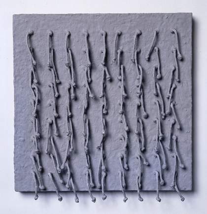 A grey, square-shaped sculpture with eighty-one short pieces of cord with knots at their ends attached to it and hanging downwards in evenly spaced rows.