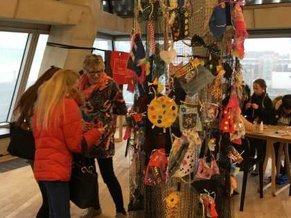 People stand and talk next to a fabric installation that hangs from the ceiling and has multicoloured pieces of textile attached to it.