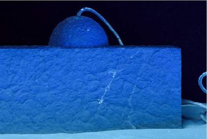 A close-up of Addendum photographed in profile to show lighter tones on the rope that emerges from one of the hemispheres, and lighter-toned, linear drips on the wood and papier mâché structure that supports it.