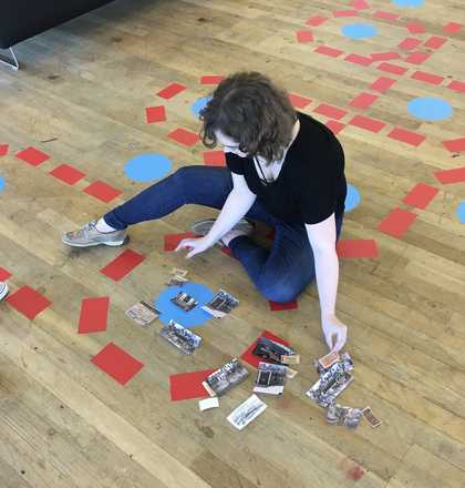 A person sits on the floor arranging pieces of coloured paper and photographs.