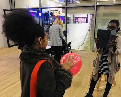 A person holds a balloon while another person photographs them using a tablet computer.