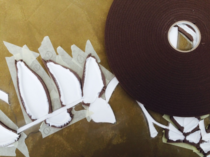 The brown surface of Double Exposure is seen from above, with a large roll of foam draught excluder on the left, surrounded by leaf and stalk shapes made of paint, draught excluder and masking tape.