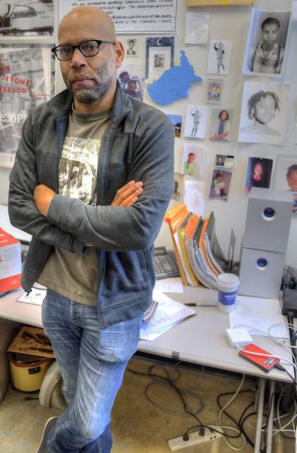 Portrait of a man standing up in front of a desk with his arms folded