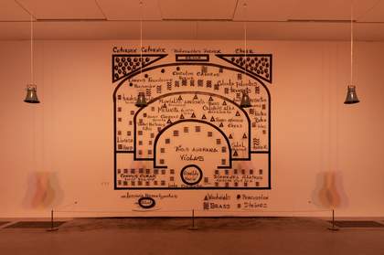 Installation by Oswaldo Macio showing 4 silver bells hanging from the ceiling. Behind is a mural of black text and lines painted directly on the gallery wall.