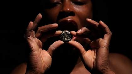 Portrait close up of a person holding up a stone to their open mouth