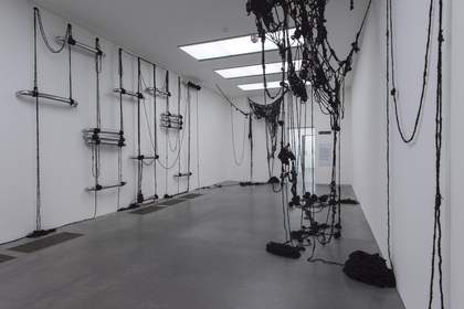 Installation shot showing strings of black human hair draping from the walls and ceiling in a gallery space at Tate Modern