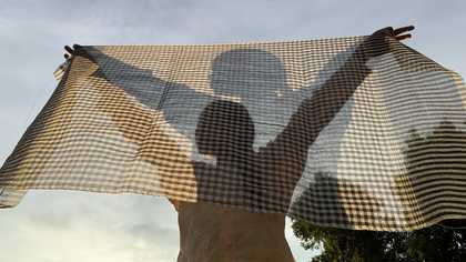 A woman stands behind a thin sheet of material
