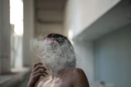 Close-up film still of a woman smoking, whose face is obscured by cigarette smoke